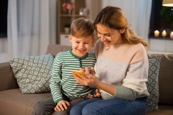 family, technology and people concept - happy smiling mother and little son sitting on sofa and using smartphone at home. mother and son using smartphone at home