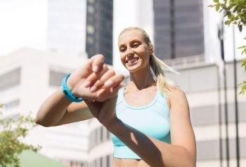 sport, technology and people concept - smiling young woman with fitness tracker and earphones exercising over city street on background. happy woman with fitness tracker and earphones