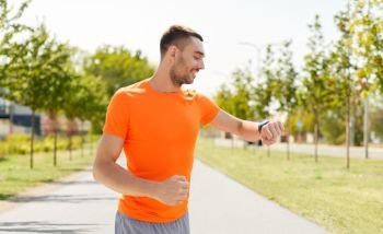 sport, technology and people concept - smiling young man with smart watch or fitness tracker running along road on city street background. smiling man with smart watch running outdoors
