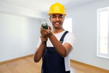 profession, construction and building - happy smiling indian worker or builder in helmet with electric drill or perforator over empty home or apartment room background. happy indian builder in helmet with electric drill