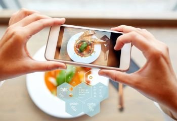 food, eating, technology, culinary and people concept - close up of hands with gazpacho soup on smartphone screen and nutritional value chart at restaurant. hands with phone and food nutritional value chart