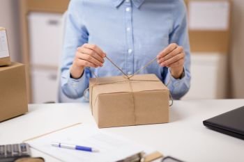 delivery, mail service, people and shipment concept - close up of woman packing parcel box and tying rope at post office. woman packing parcel and tying rope at post office