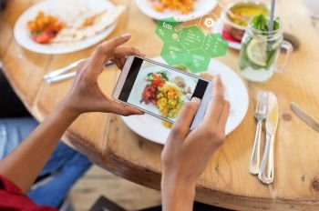 technology, eating and people concept - hands with smartphone photographing food at restaurant over nutritional value chart. hands with smartphone and food at restaurant