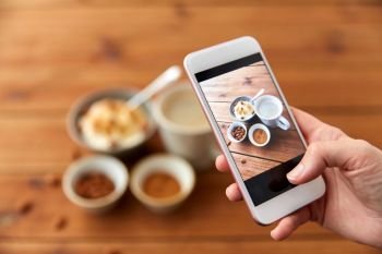 food, eating and breakfast concept - hand of woman taking picture of porridge in bowl, almond nuts, cinnamon and cup of coffee on wooden table with smartphone. hand taking picture of breakfast with smartphone