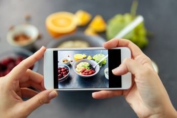 food, eating and breakfast concept - hand of woman taking picture of cereals in bowl with fruits, berries and juice with smartphone. hands taking picture of breakfast with smartphone