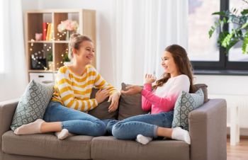 people and friendship concept - happy teenage girls sitting on sofa and talking at home. happy teenage girls talking on sofa at home