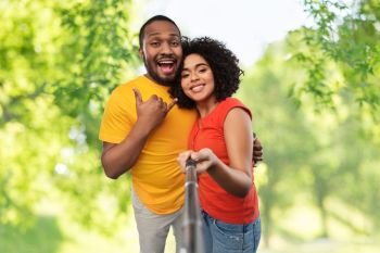 relationships and people concept - happy african american couple taking picture by selfie stick over green natural background. african couple taking picture by selfie stick