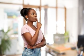 people, silence and secret concept - african american young woman with finger on lips over office background. african american woman with finger on lips