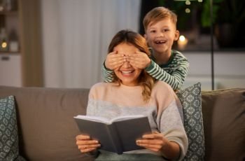 family, love and people concept - happy smiling mother with book playing game with her little son in evening. happy smiling mother playing with her son at home