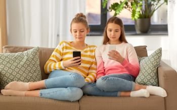 people, technology and friendship concept - teenage girls with smartphones sitting on sofa at home. girls with smartphones sitting on sofa at home