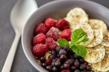 food and breakfast concept - close up of cereals in bowl with wild berries, banana and peppermint on slate stone table. cereal breakfast with berries, banana and mint