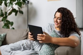 technology, leisure and people concept - happy smiling woman with tablet pc computer on sofa at home. woman with tablet pc computer on sofa at home