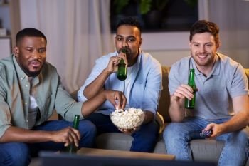 friendship, leisure and people concept - happy male friends with beer and popcorn watching tv at home at night. happy male friends with beer watching tv at home