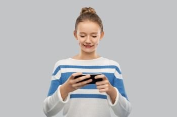 technology and people concept - happy smiling teenage girl in pullover using smartphone over grey background. happy smiling teenage girl using smartphone
