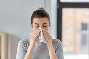 healthcare, cold, allergy and people concept - sick woman blowing her runny nose in paper tissue at home. sick woman blowing nose in paper tissue at home