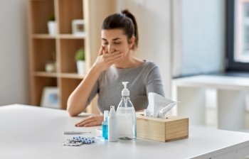 people, health and fever concept - medicines and sanitizers on table over sick woman coughing at home. medicines and sick woman coughing at home