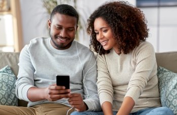 technology, music and people concept - happy african american couple with smartphone and earphones at home. happy couple with smartphone and earphones at home