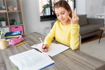 children, education and learning concept - happy student girl with book counting fingers and writing to notebook at home. student girl with book writing to notebook at home