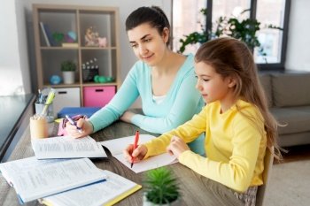education, family and homework concept - happy mother and daughter with book writing to notebook at home. mother and daughter doing homework together