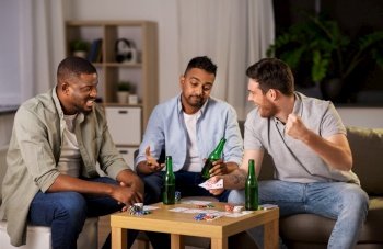 leisure games, friendship and gambling concept - male friends playing cards and drinking beer at home at night. male friends playing cards at home at night