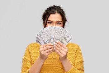 finance, investment and saving concept - young woman covering her face with fan of dollar money over grey background. young woman covering her face with dollar money