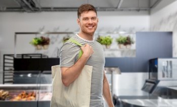 sustainability, consumerism and eco friendly concept - happy smiling man with reusable canvas bag for food shopping over store background. man with reusable canvas bag for food shopping