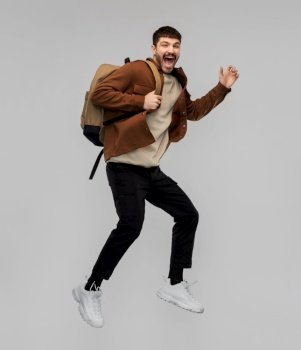 travel, tourism and people concept - happy smiling young man with backpack jumping in air over grey background. smiling young man with backpack jumping in air