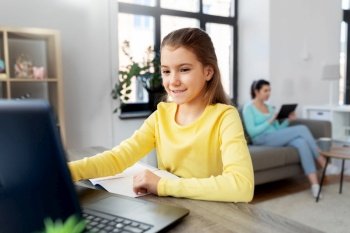 children, education and distant learning concept - smiling student girl with laptop computer and notebook and mother with tablet pc at home. student girl with laptop learning online at home