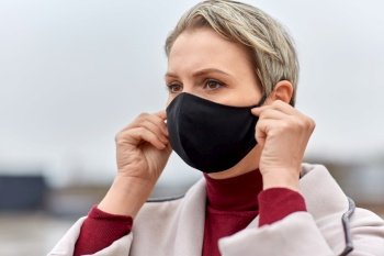 health, safety and pandemic concept - young woman wearing black face protective reusable barrier mask outdoors. woman wearing protective reusable barrier mask