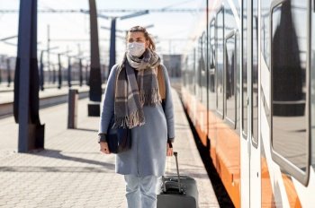 health, safety and pandemic concept - young woman in protective face mask with travel bag walking along empty railway station. woman in protective face mask at railway station