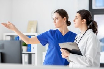 medicine, healthcare and people concept - nurse showing something to doctor with clipboard at hospital. nurse showing something to doctor at hospital