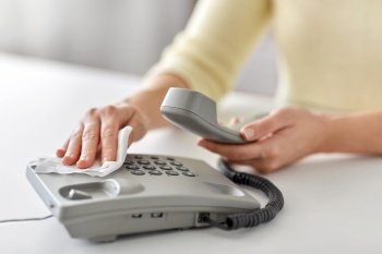 hygiene and disinfection concept - close up of woman hands cleaning desk phone with paper tissue. close up of woman cleaning desk phone with tissue