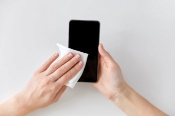 hygiene and disinfection concept - close up of woman hands cleaning smartphone with tissue. close up of hands cleaning smartphone with tissue