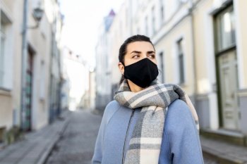 health, safety and pandemic concept - young woman wearing black face protective reusable barrier mask in city. woman wearing protective reusable mask in city