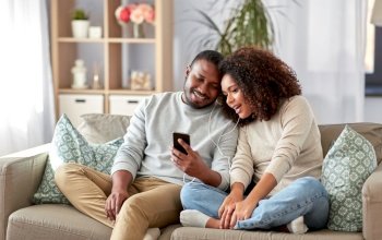 technology, music and people concept - happy african american couple with smartphone and earphones at home. happy couple with smartphone and earphones at home