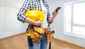 repair, construction and building concept - woman or builder with smartphone, helmet and working tools on belt over empty room at new home background. woman or builder with phone and working tools