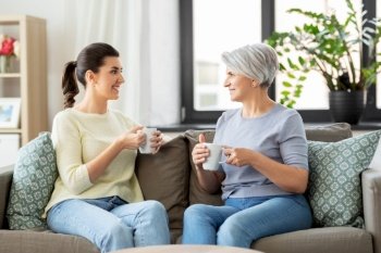 family, generation and people concept - happy smiling senior mother with adult daughter drinking coffee or tea and talking at home. senior mother and adult daughter drinking coffee
