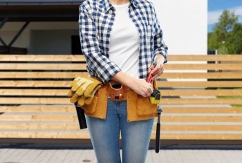 repair, construction and building concept - woman or builder with pliers and working tools on belt over living house background. woman or builder with working tools on belt