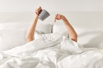 morning, comfort and people concept - young woman with cup of coffee lying in bed at home bedroom. woman with cup of coffee lying in bed