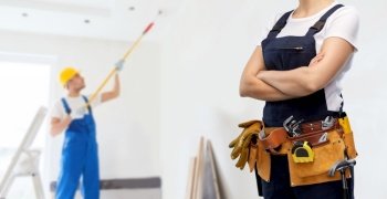 repair, construction and building concept - woman or builder with working tools on belt over painter painting ceiling background. woman or builder with working tools on belt