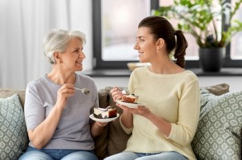 family, generation and people concept - happy smiling senior mother and adult daughter eating cake at home. old mother and adult daughter eating cake at home