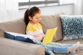childhood and leisure concept - happy smiling little girl reading book at home. happy smiling little girl reading book at home