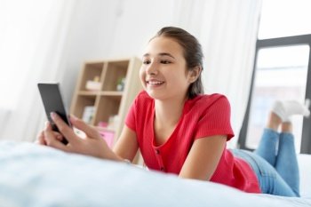 children, technology and communication concept - smiling teenage girl texting on smartphone at home. smiling teenage girl texting on smartphone at home