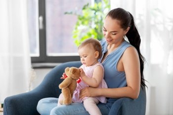 family, child and motherhood concept - portrait of happy smiling mother and little baby daughter with teddy bear toy sitting in chair at home. happy mother with little baby daughter at home