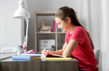 children, education and learning concept - student teenage girl with book writing to notebook at home. student girl with book writing to notebook at home