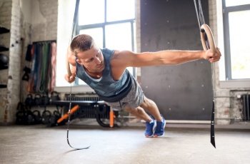 fitness, sport, bodybuilding and people concept - young man exercising on gymnastic rings in gym. man doing exercising on gymnastic rings in gym
