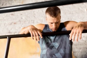 fitness, sport, training and lifestyle concept - tired young man exercising on parallel bars in gym. tired young man at parallel bars in gym