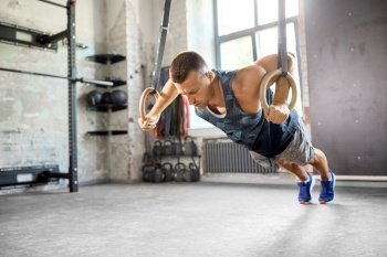 fitness, sport, bodybuilding and people concept - young man doing push-ups on gymnastic rings in gym. man doing push-ups on gymnastic rings in gym
