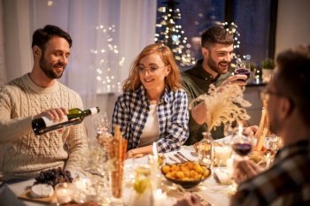 holidays and celebration concept - happy friends having christmas dinner at home pouring red wine. happy friends with red wine at christmas party