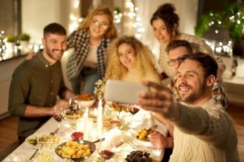 holidays, celebration and people concept - happy friends taking selfie with smartphone at home christmas dinner party. friends taking selfie at christmas dinner party